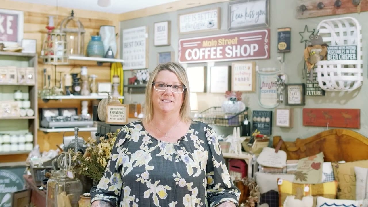 Woman standing in a cozy coffee shop filled with rustic decor and various items on display